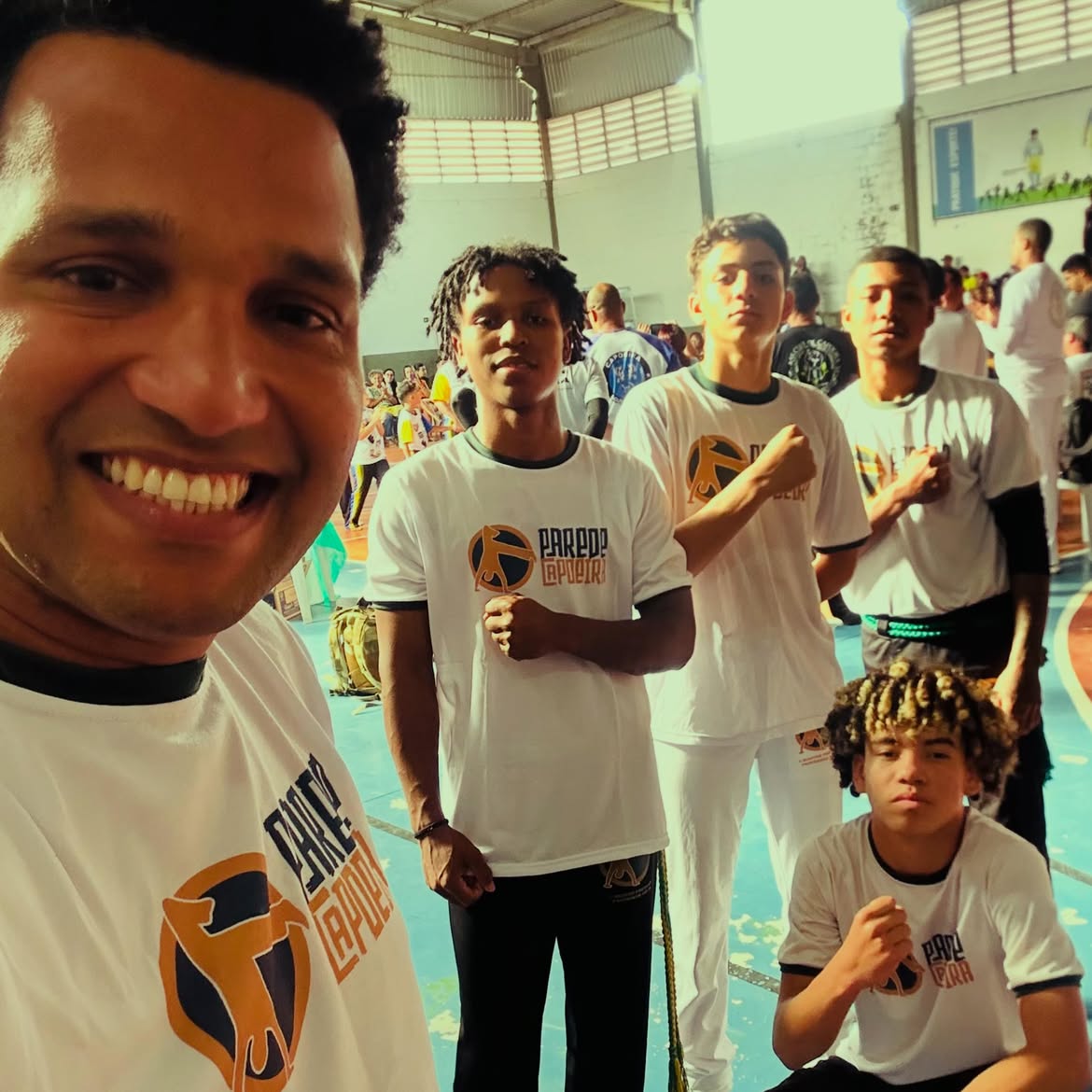 Alunos do Parede Capoeira com uniforme branco durante evento em ginásio